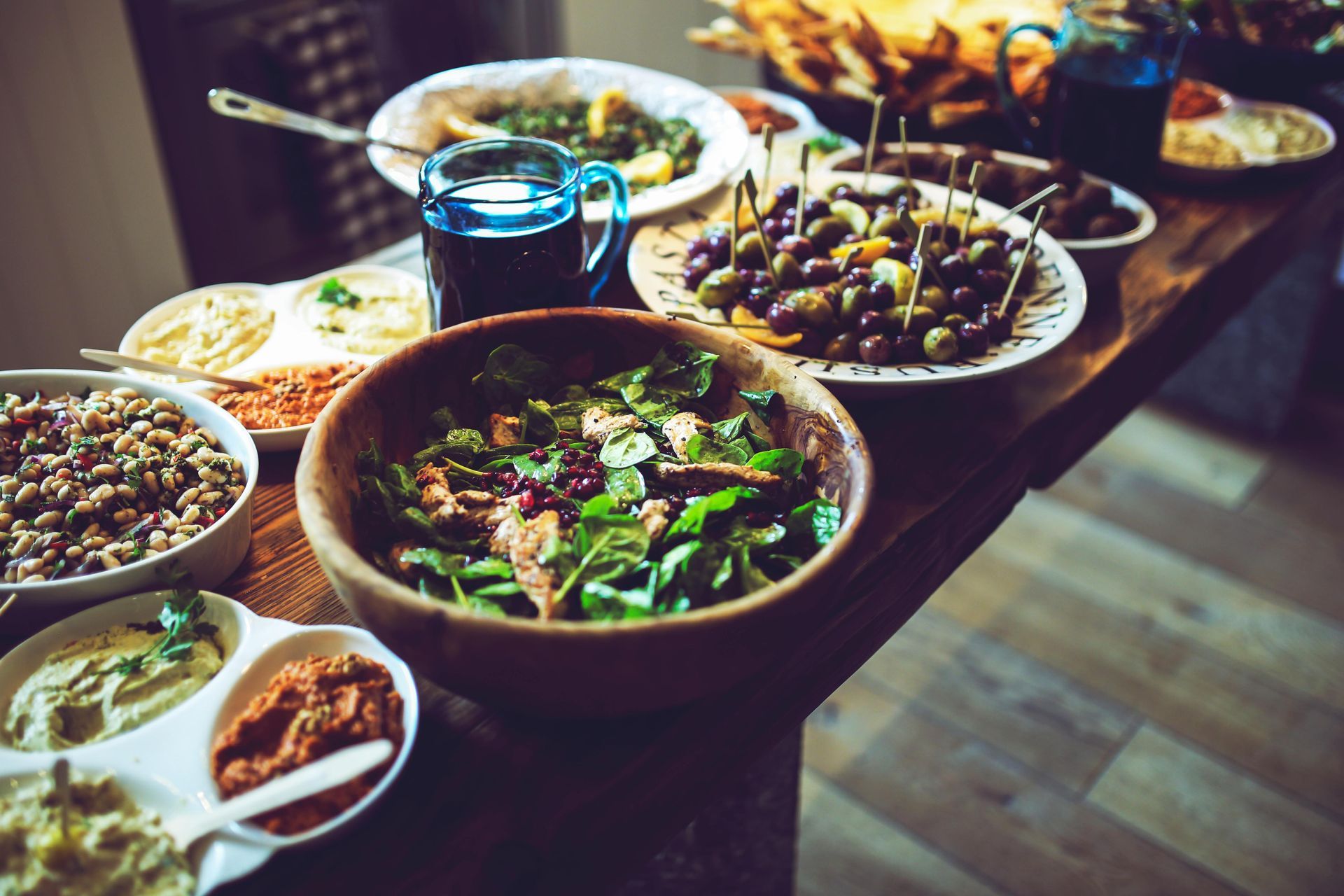 Table laden with various dishes, including salad, olives, dips, and a blue glass of beverage.