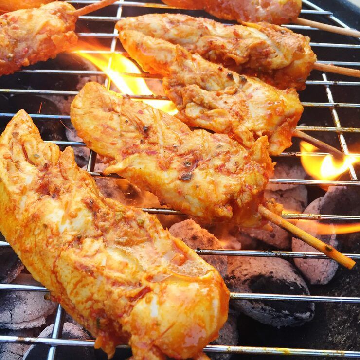 Chicken skewers grilling over charcoal. Flames visible.