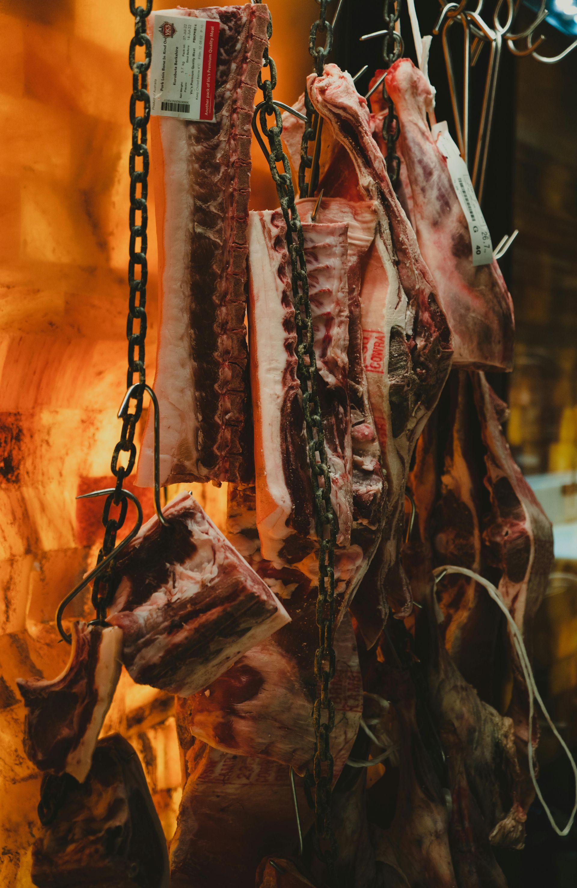 Chains suspending various cuts of raw meat, likely beef, in a butcher shop. Some cuts show bone.