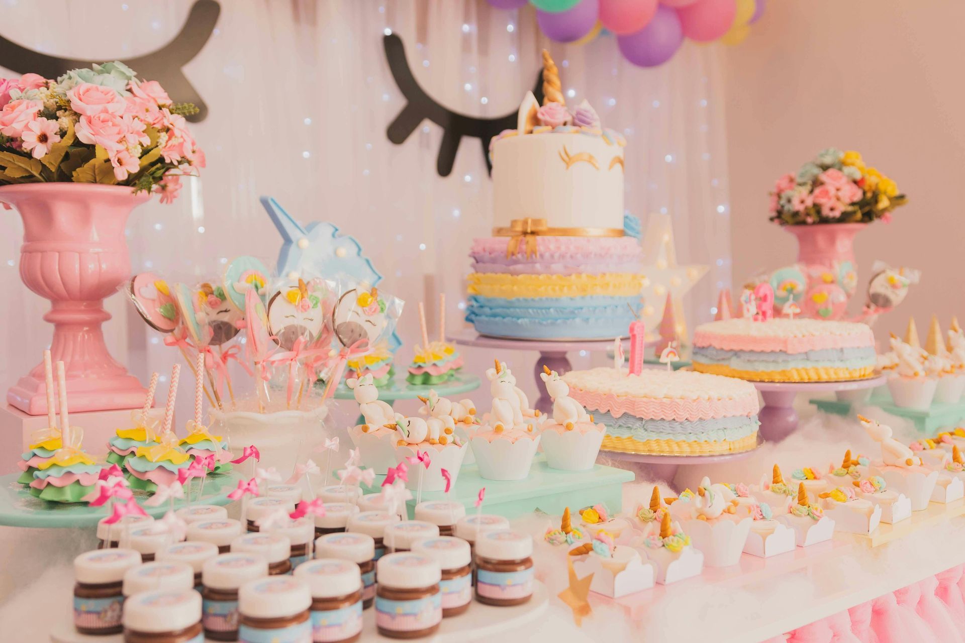 Unicorn-themed dessert table with cakes, sweets, and decorations in pastel colors.