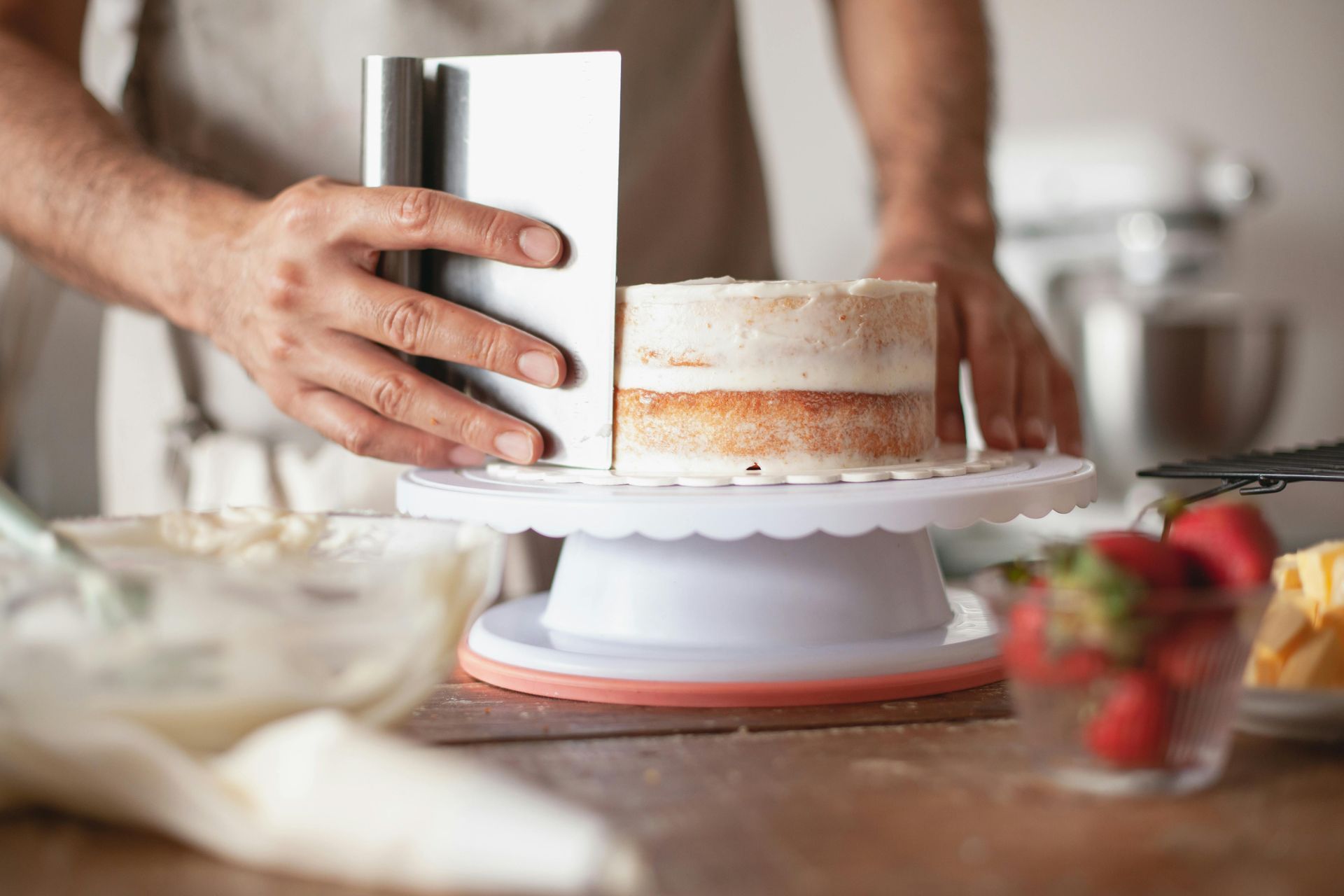 Baker smoothing frosting on a cake with a scraper on a rotating stand