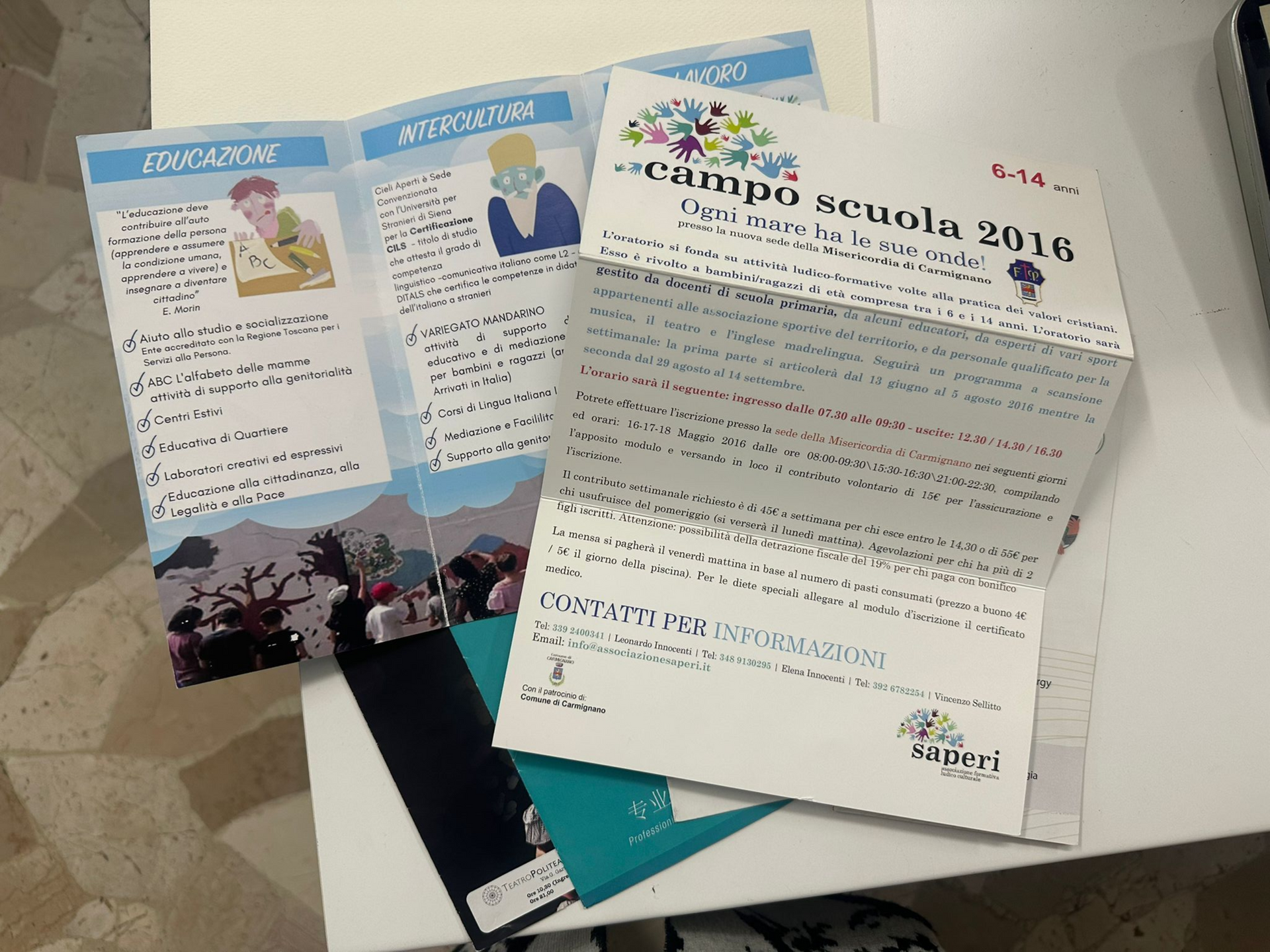 Opuscolo e lettera su un evento scolastico disposti su un tavolo. Contengono testo e illustrazioni.
