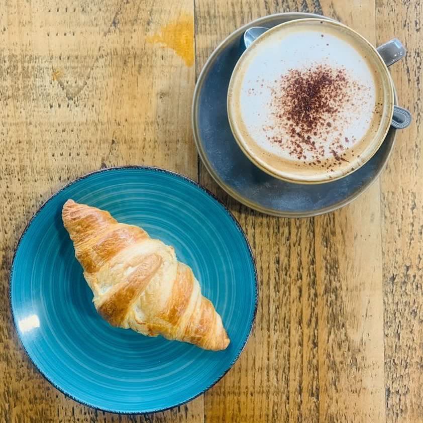 a croissant on a blue plate next to a cup of coffee
