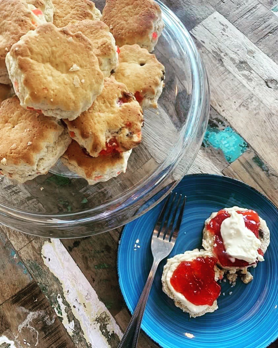a plate of scones with jam and whipped cream next to a bowl of scones .