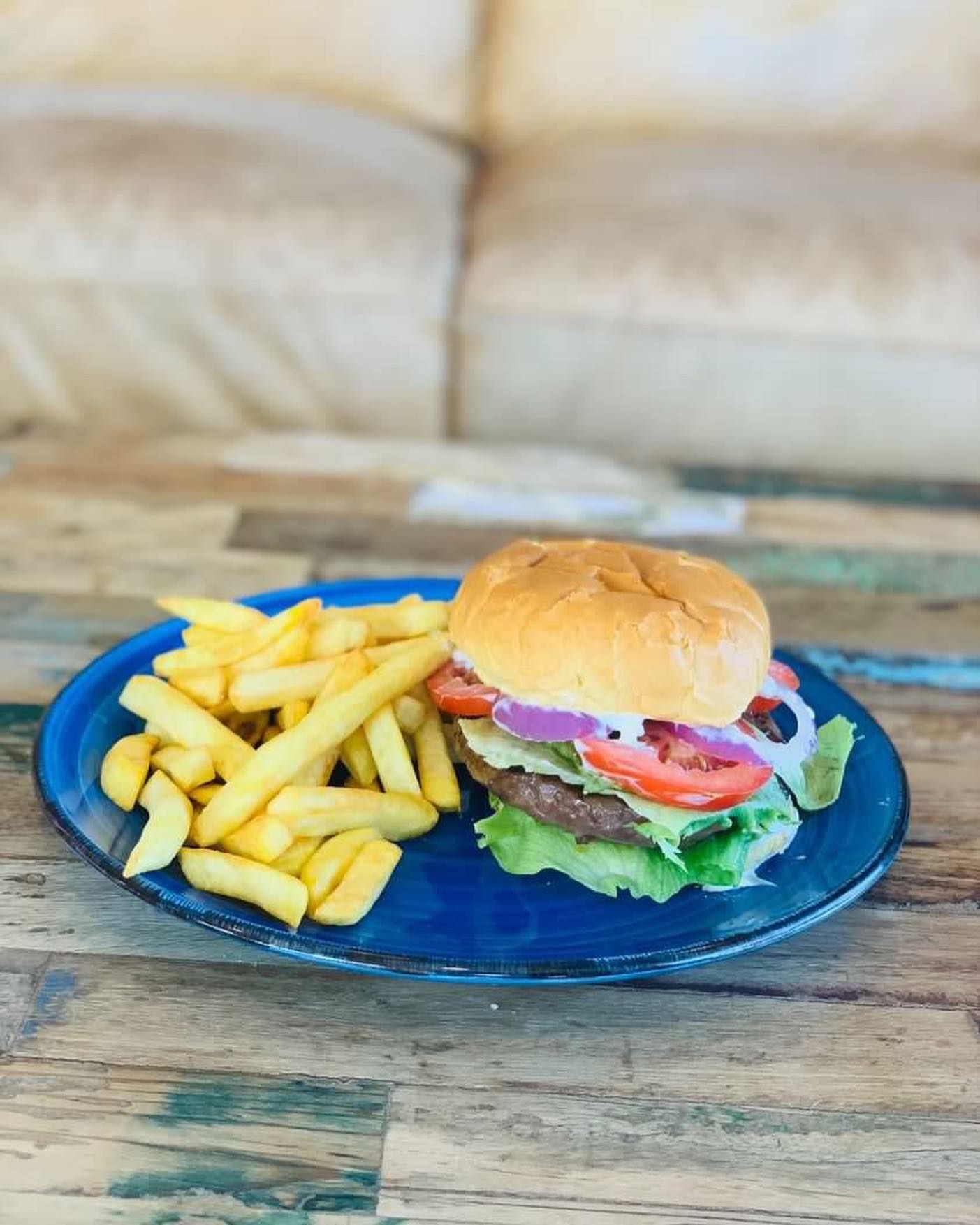 a blue plate topped with a hamburger and french fries on a wooden table .