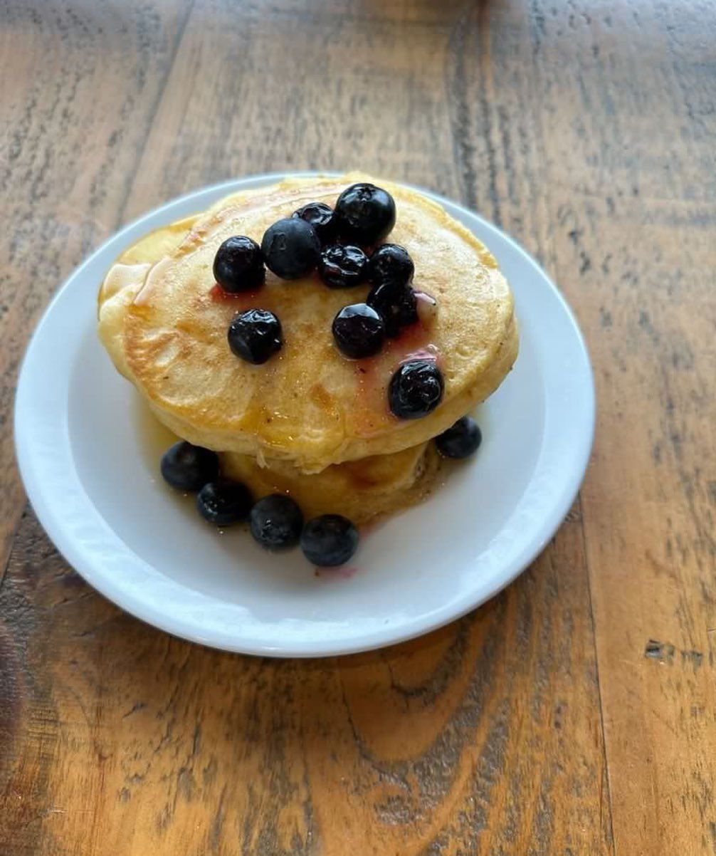 a stack of pancakes with blueberries on a white plate on a wooden table .