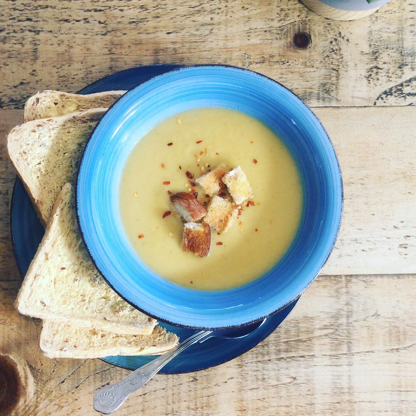 a bowl of soup with croutons and toast on a wooden table