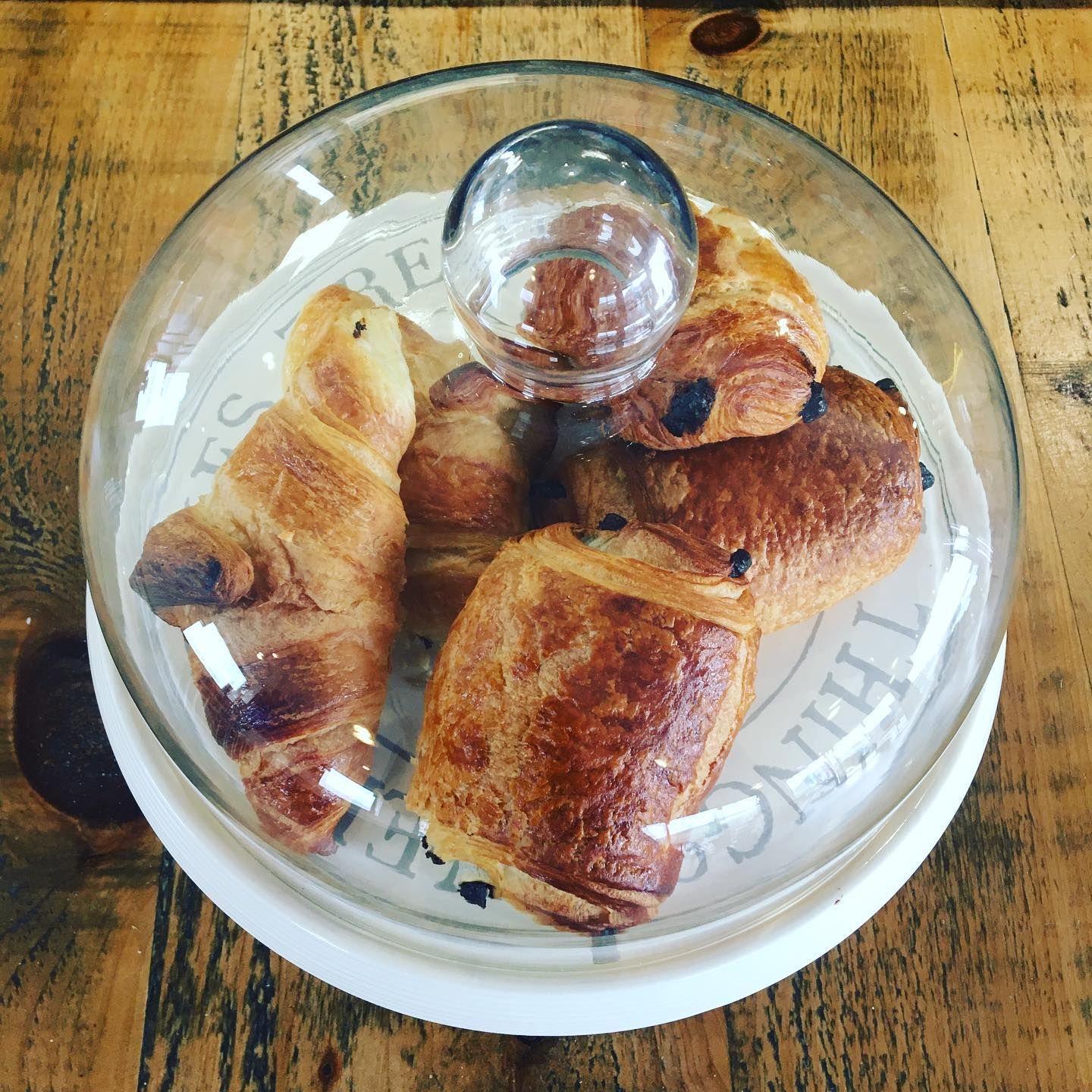 a glass dome filled with croissants and pastries on a wooden table .