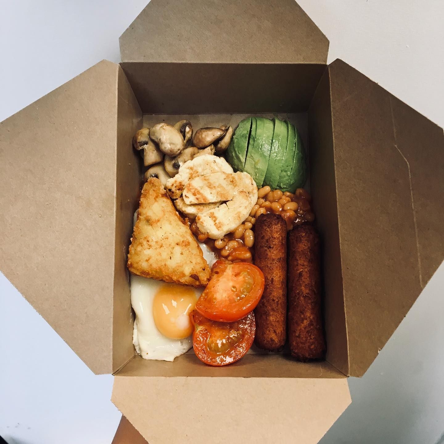 a cardboard box filled with food including eggs tomatoes and sausages