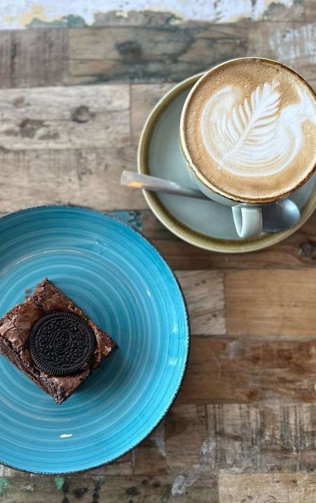 a brownie and a cup of cappuccino are on plates on a wooden table .
