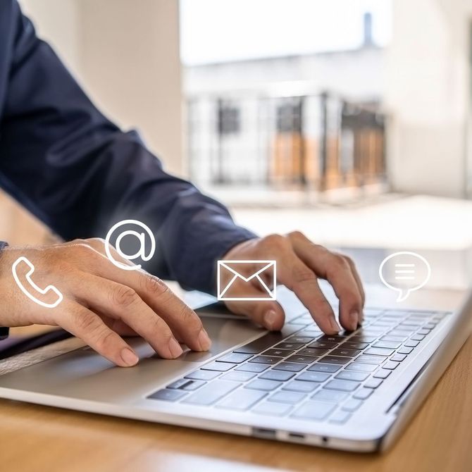 A person is typing on a laptop with a phone email and speech bubble icons