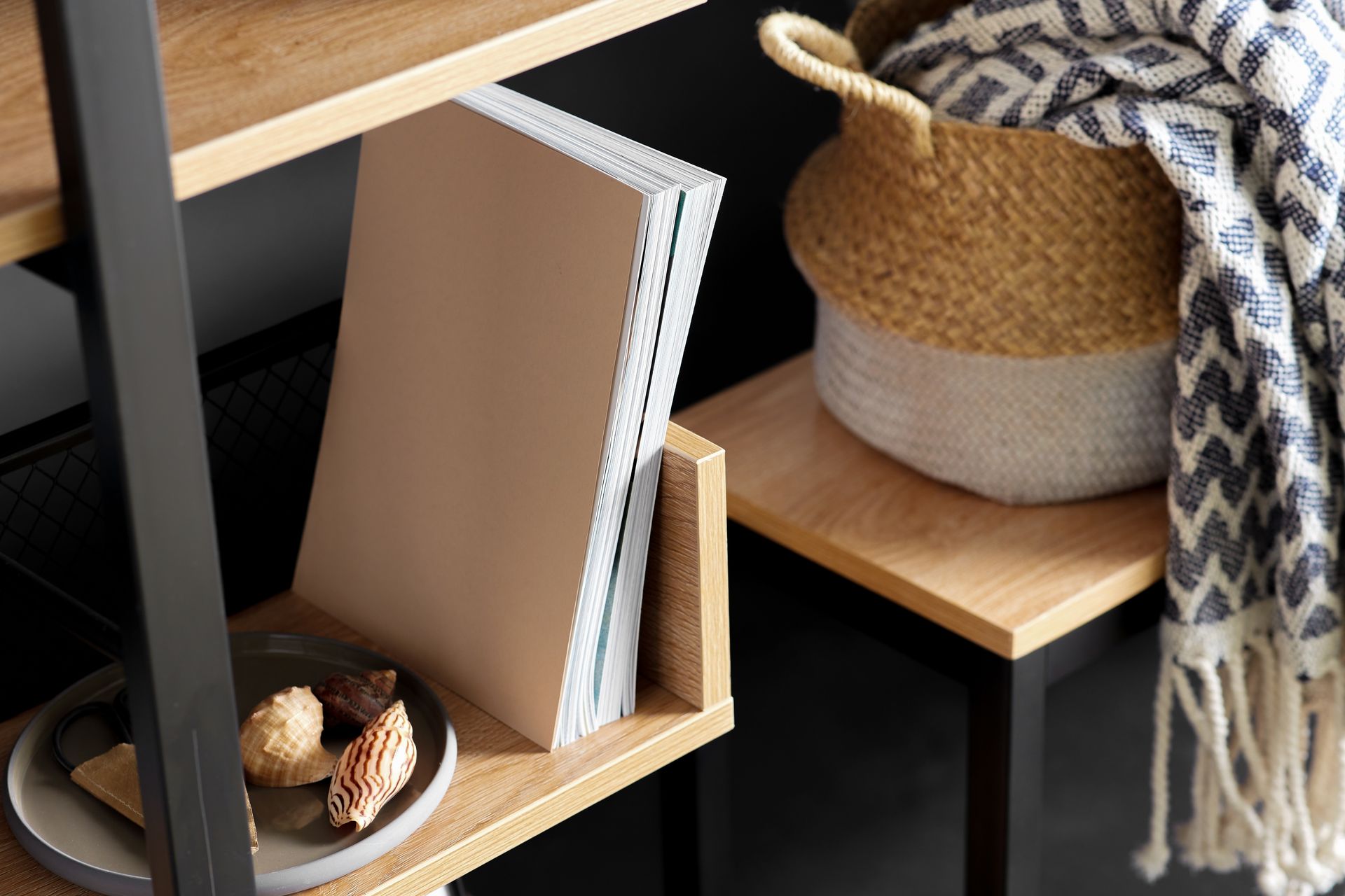 A bookshelf with books , a basket and a blanket on it.