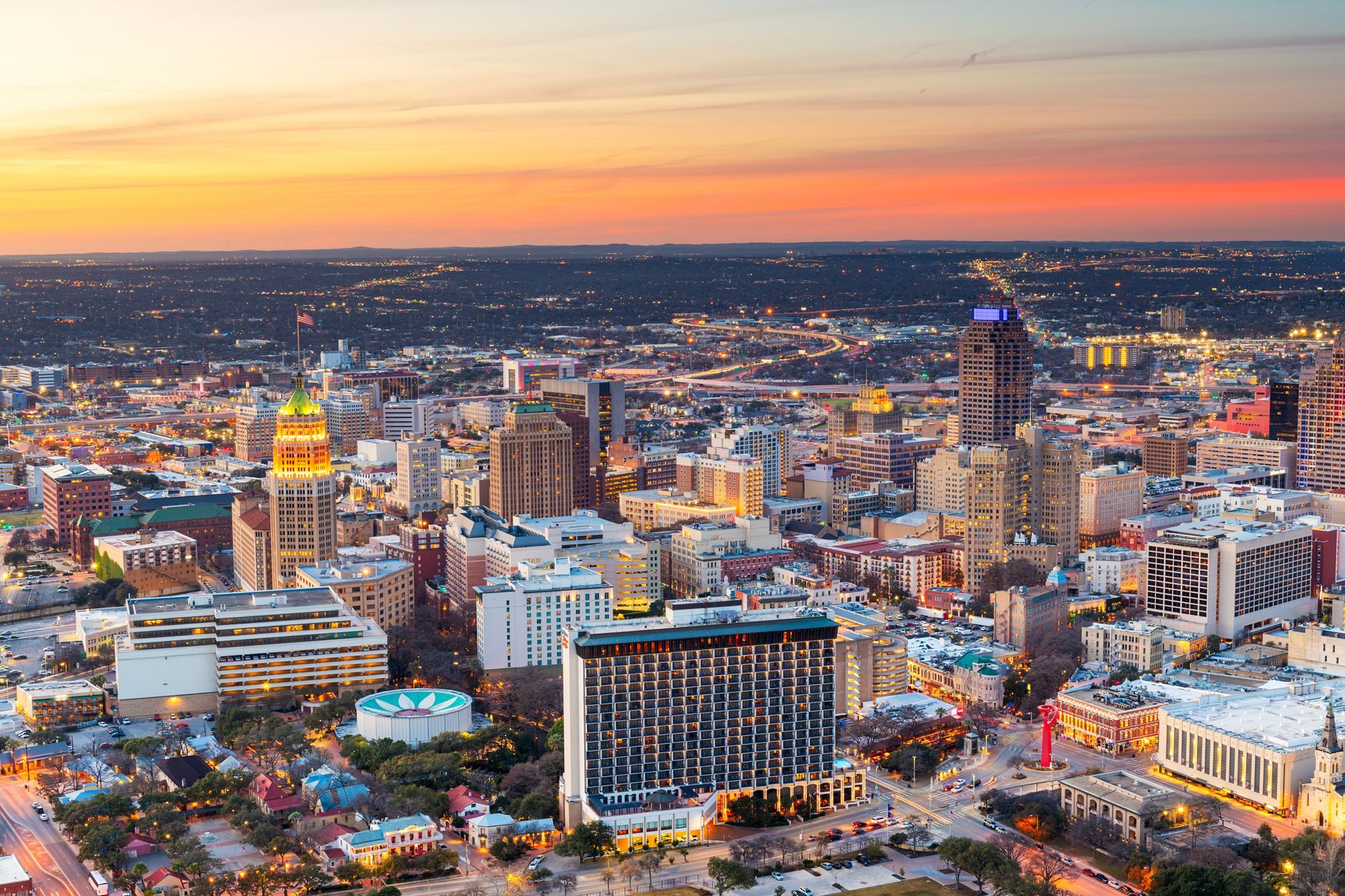 City skyline at sunset with illuminated buildings and colorful sky.