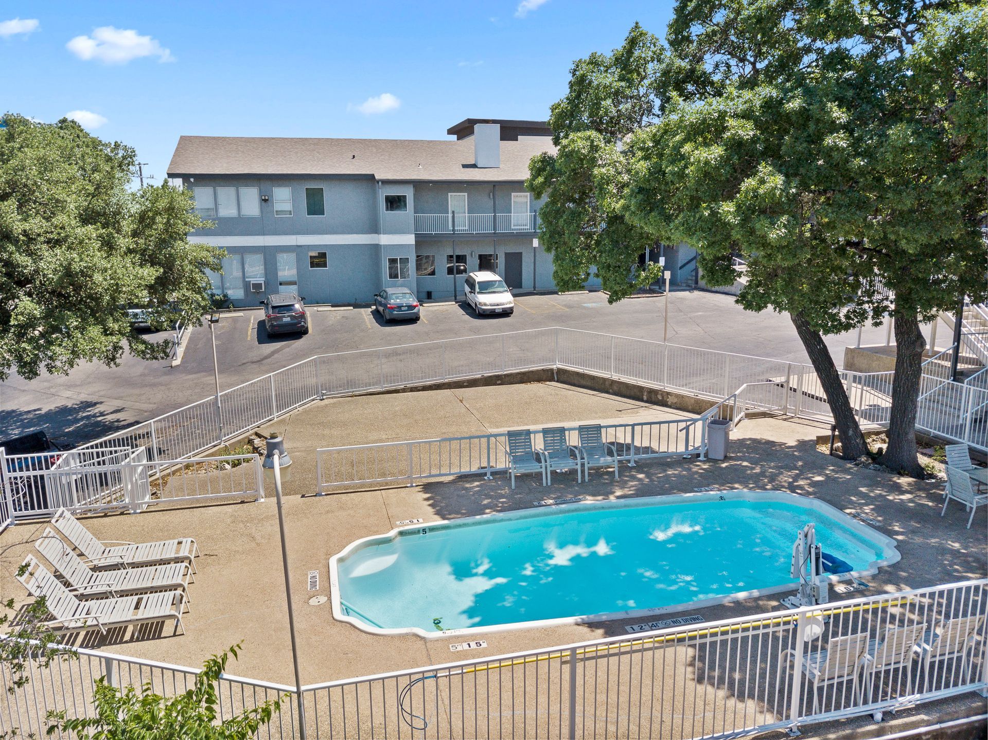 Exterior of a two-story motel with a pool and parking lot on a sunny day.