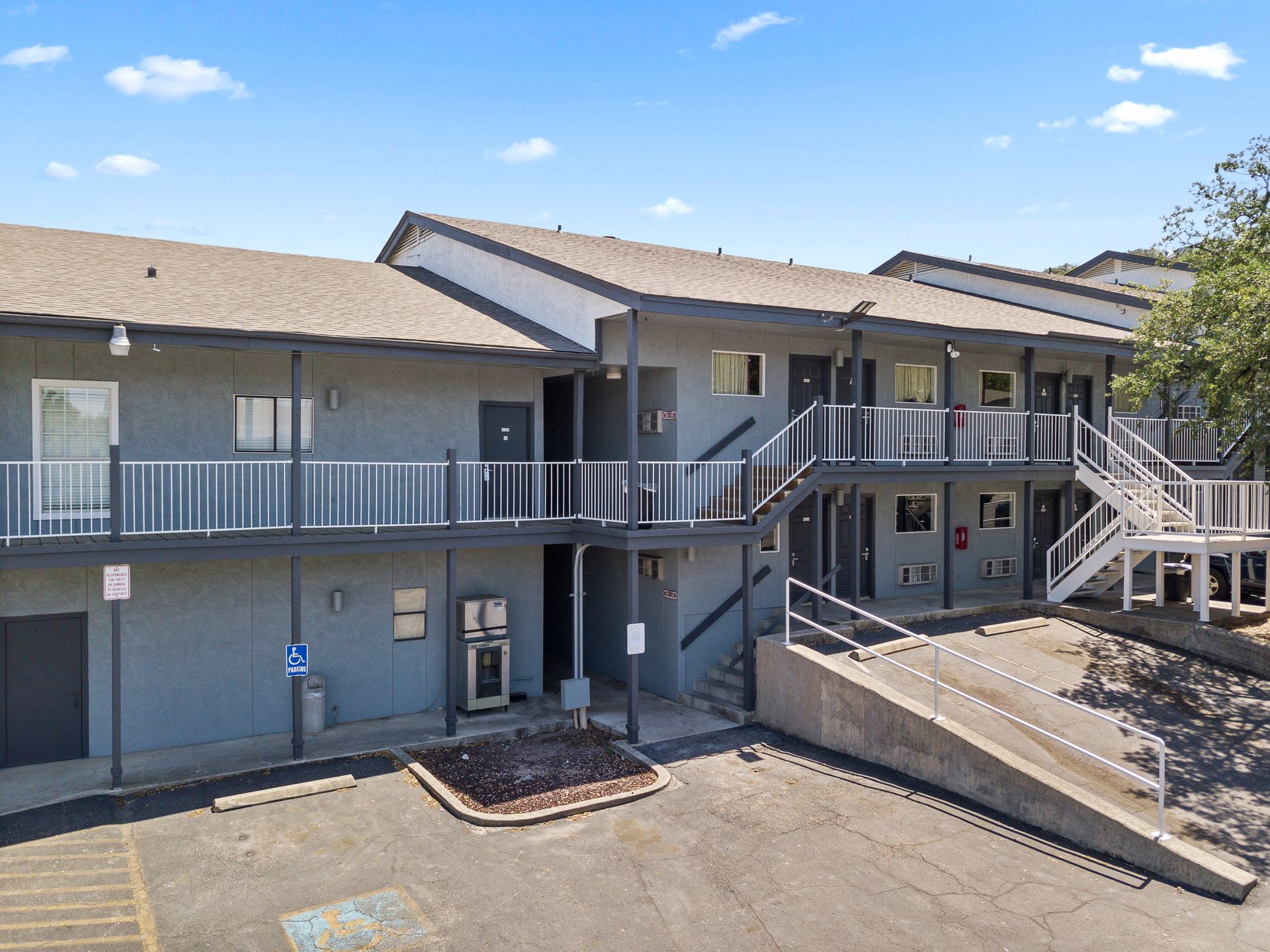 Gray two-story apartment building with exterior stairs and balconies, with a blue sky background.