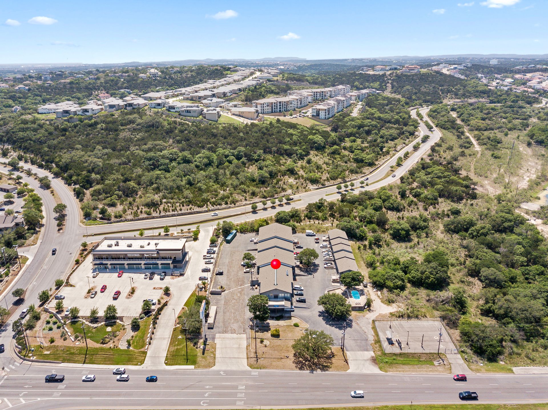 Aerial view of a building complex with a road in front and trees in the background under a blue sky.