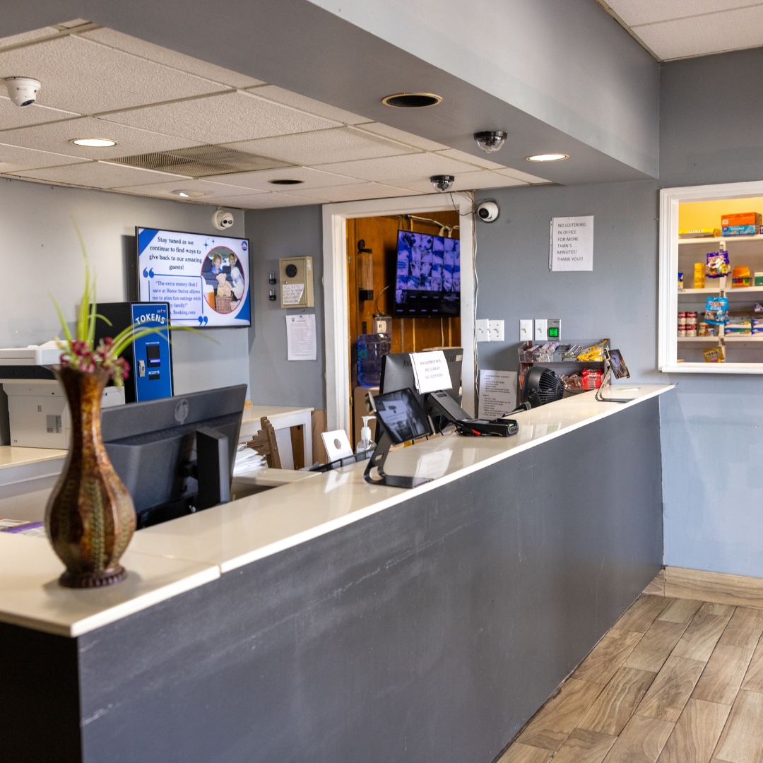 Reception desk in a gray-walled office. A monitor displays a graphic. A vase sits on the counter.