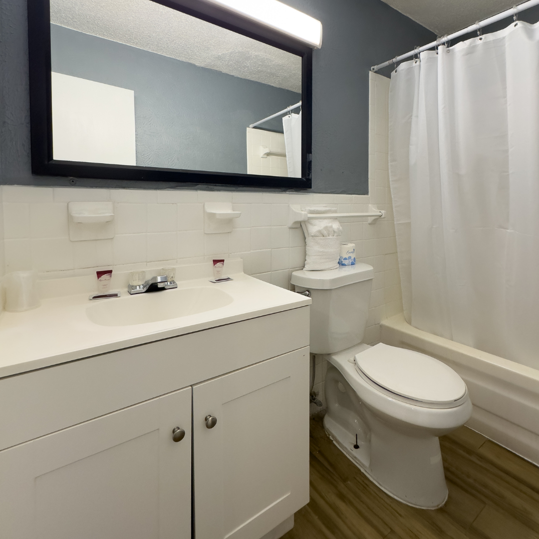 White bathroom with vanity, toilet, and shower/tub. Mirror over the vanity.