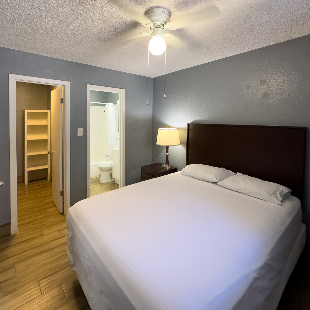 Bedroom with a bed, nightstand, and doors to bathroom and storage. The room has a ceiling fan and hardwood floor.