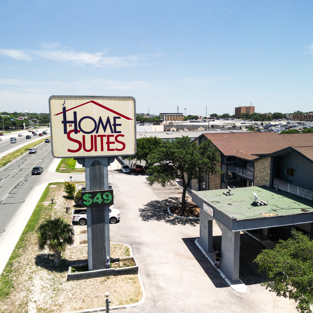 Home Suites hotel sign with price. Road, parking area, buildings, and sky in the background.