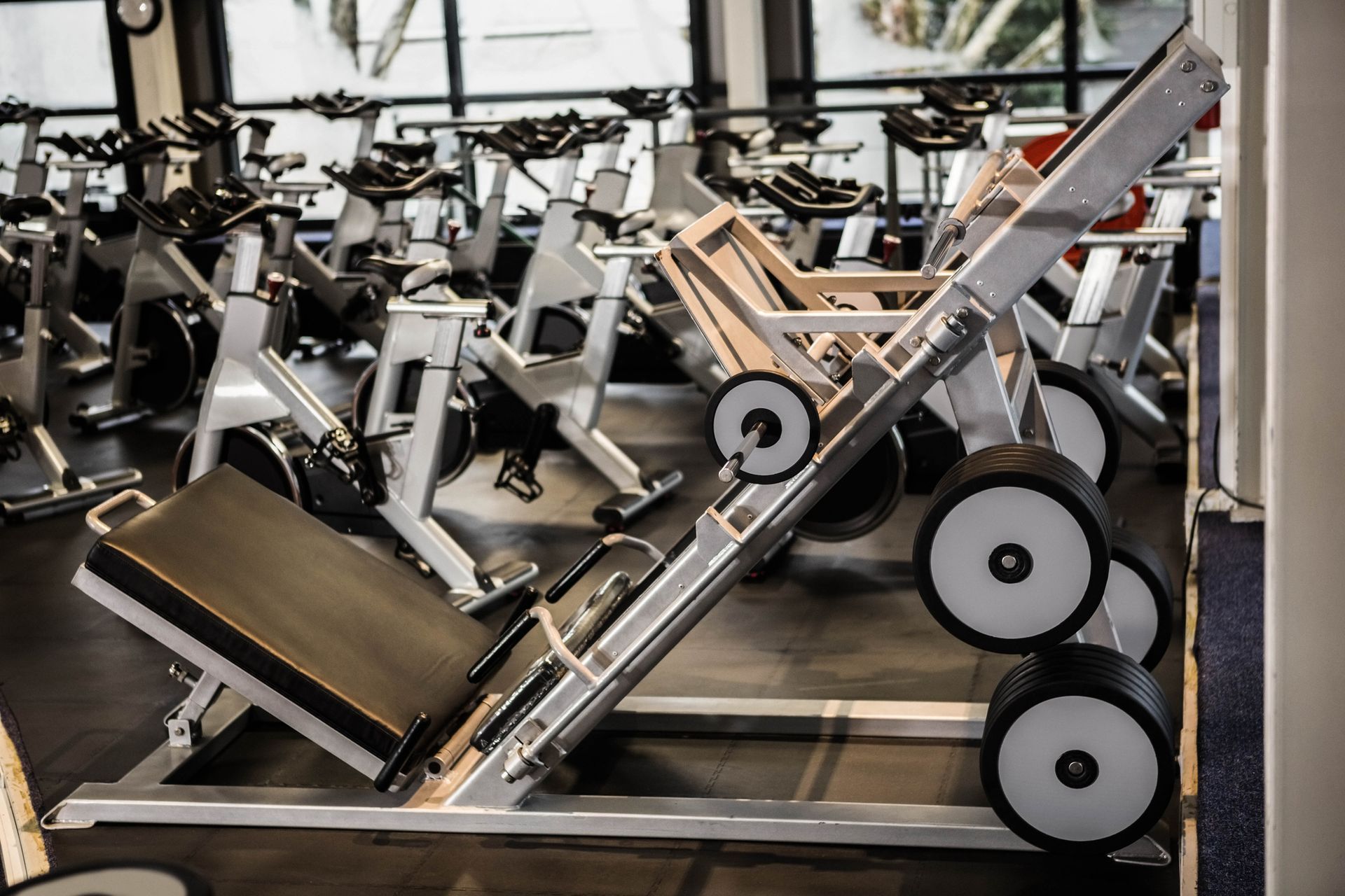 Máquinas industriales de prensa de piernas alineadas en un gimnasio, con estructuras plateadas y asientos acolchados negros.