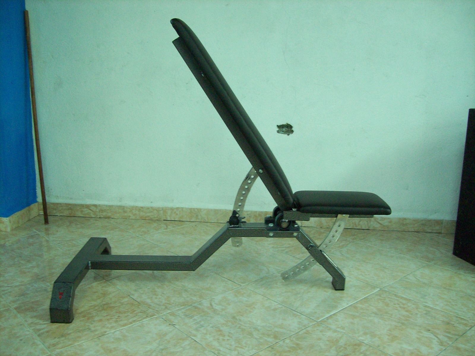 Banco de ejercicios negro ajustable con soporte para las piernas en un gimnasio con suelo de baldosas.