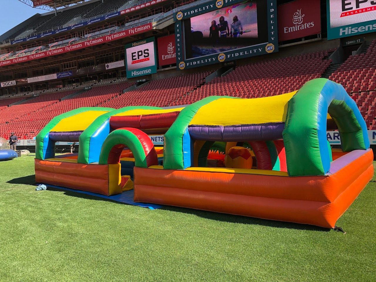 A large inflatable obstacle course is sitting on the grass in front of a stadium.