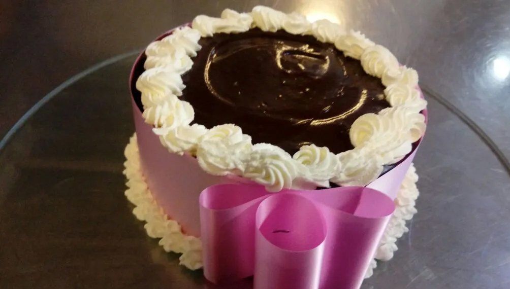 Torta al cioccolato con glassa bianca, ricoperta di glassa al cioccolato e legata con un nastro rosa.
