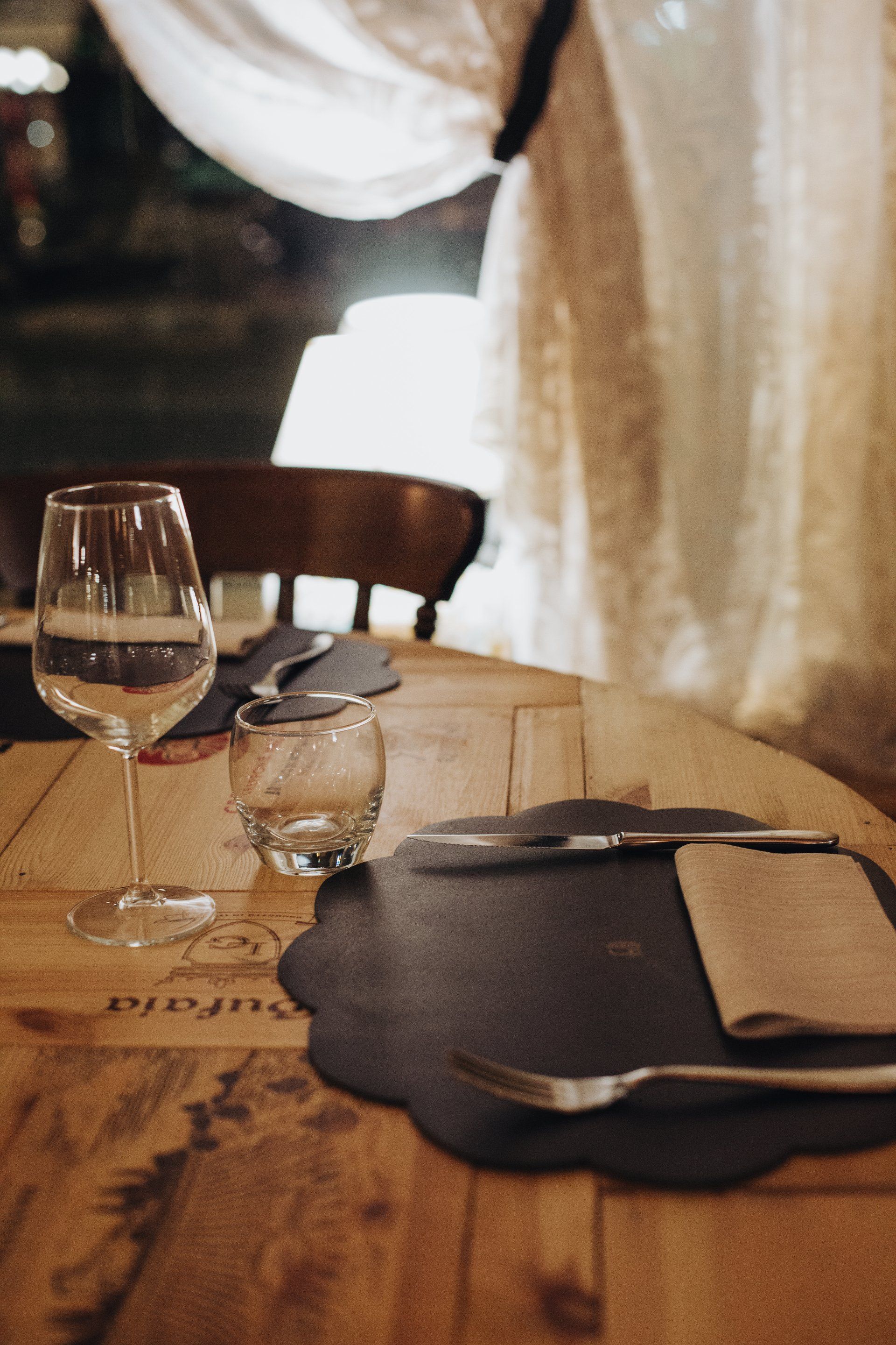 Set da tavola in legno per cenare: calice da vino, bicchiere piccolo, tovaglietta nera, posate, tovagliolo.