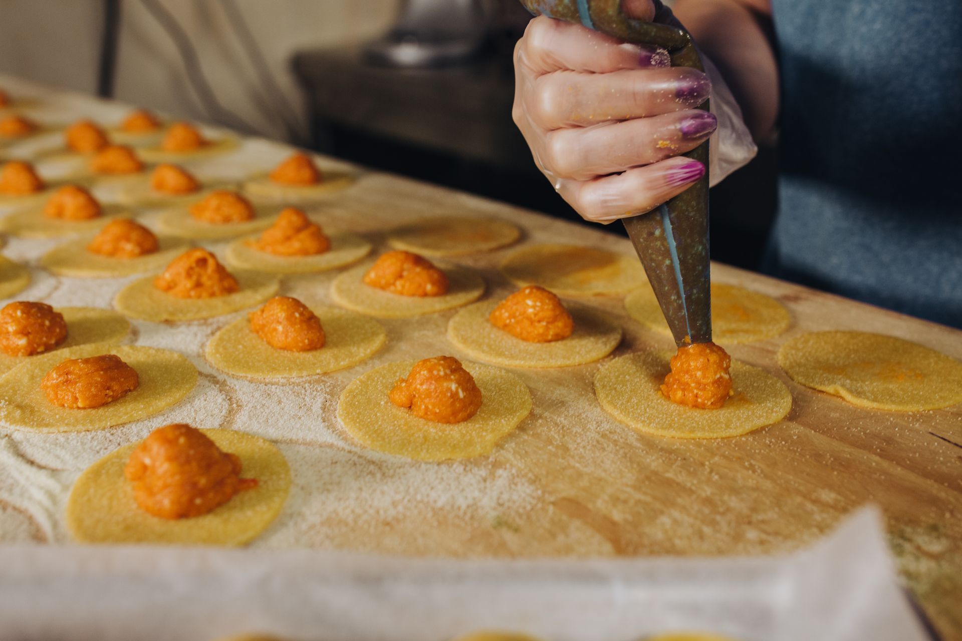 Una mano versa il ripieno all'arancia sui cerchi di pasta su una superficie di legno, preparando i ravioli.