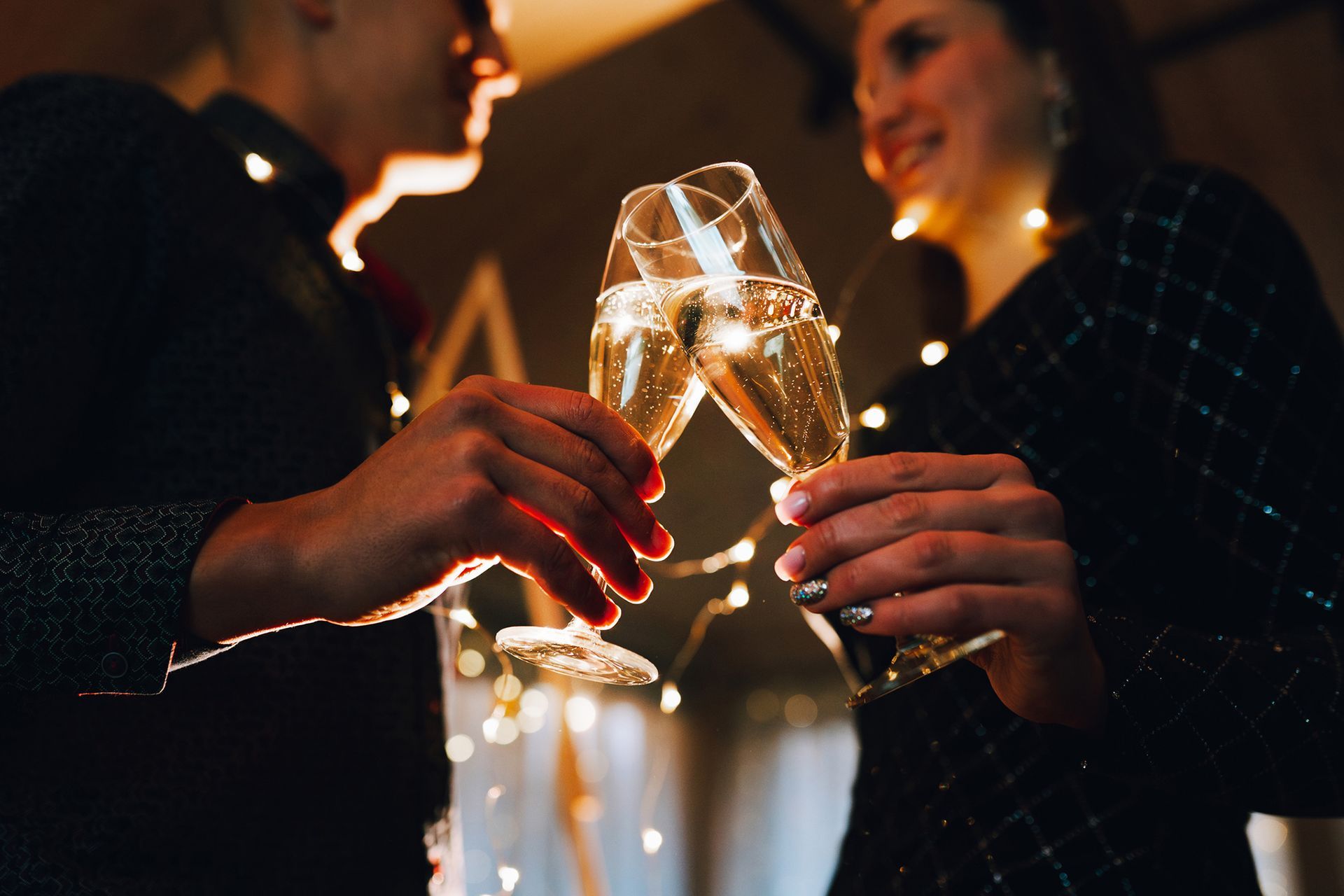 Una coppia brinda con calici da champagne, illuminati da luci calde.