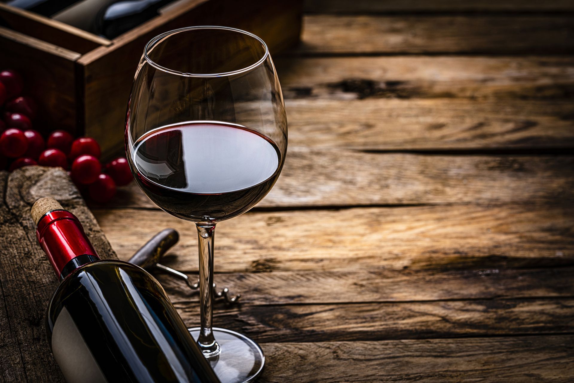 Bottiglia di vino rosso e bicchiere su una superficie di legno, con uva e un cavatappi.