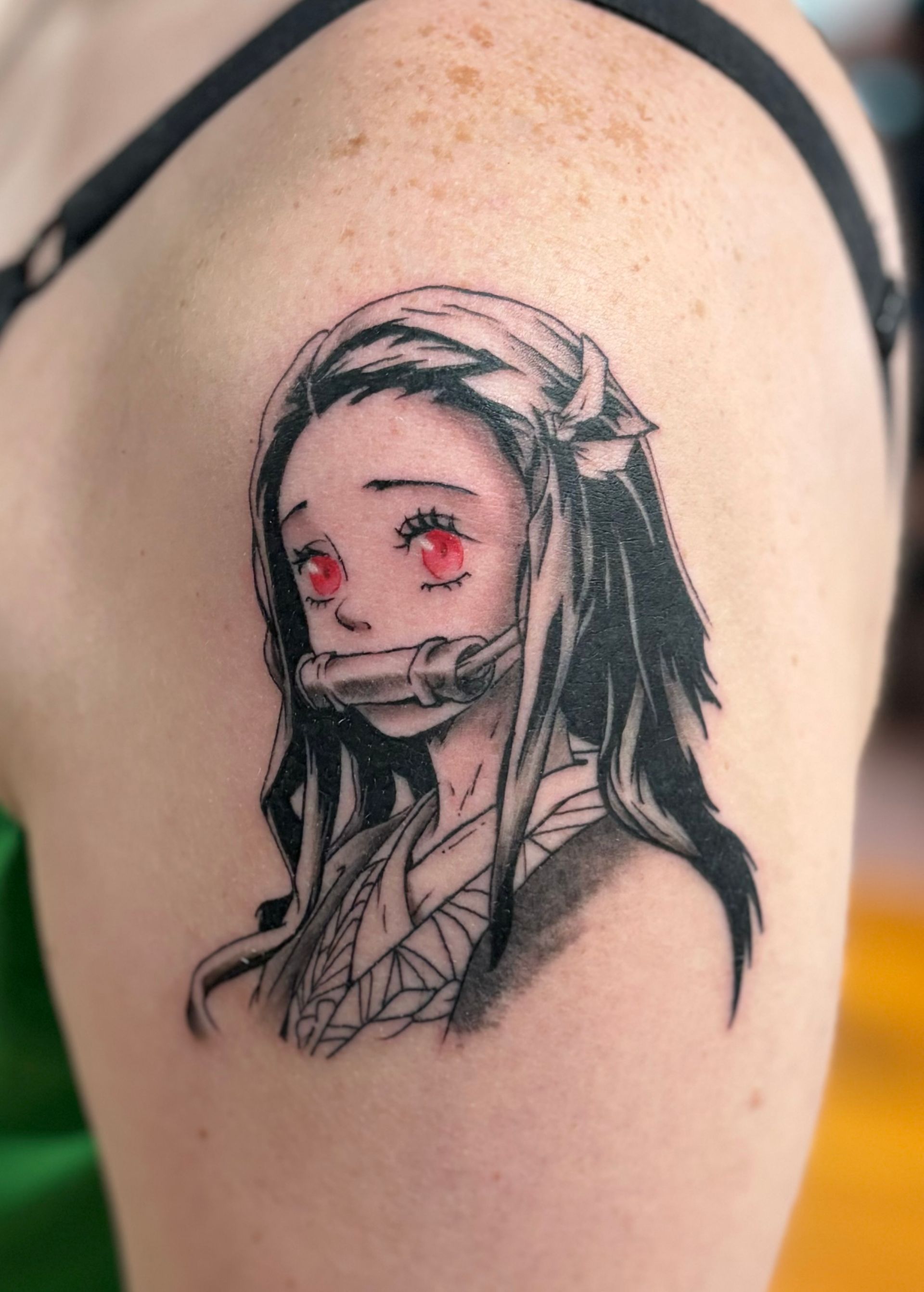 Tattoo of Nezuko from Demon Slayer. Black ink, red eyes, bamboo muzzle, on a shoulder.