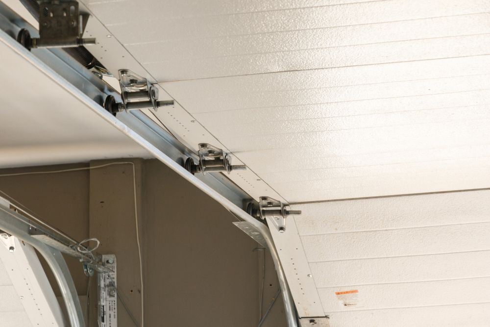 A low-angle view showing the interior track, rollers, and metal hinges of a white garage door in a closed position.