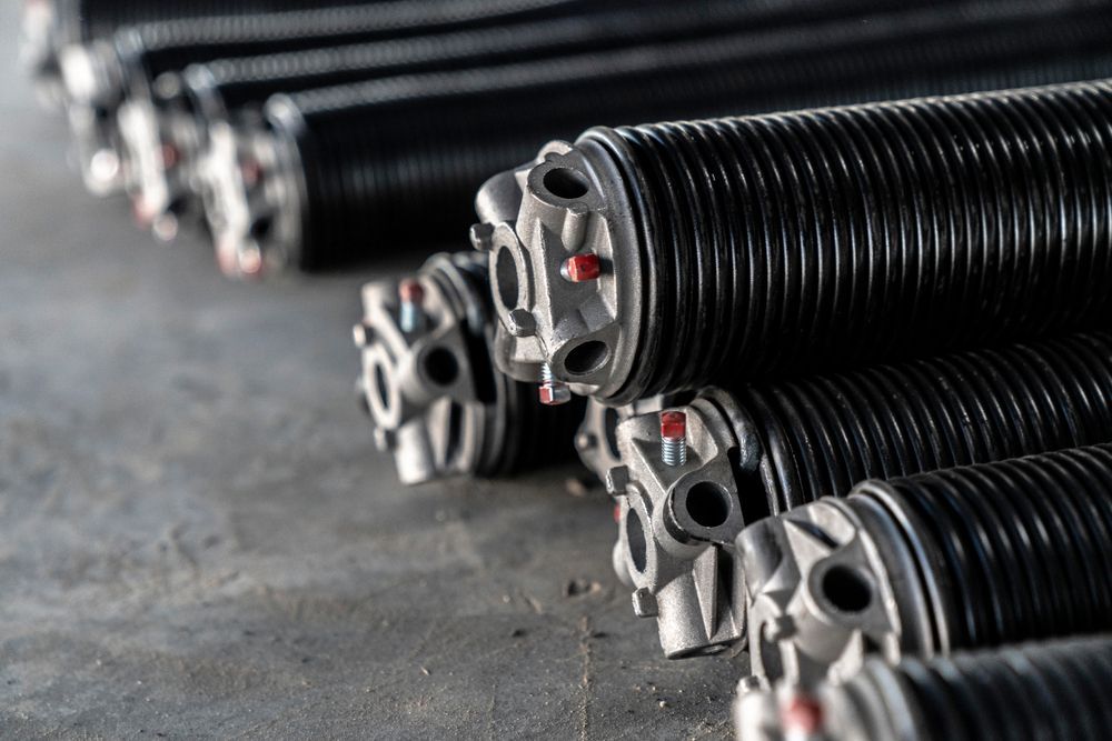 A collection of black metal torsion springs for garage doors, arranged in rows on a concrete floor.