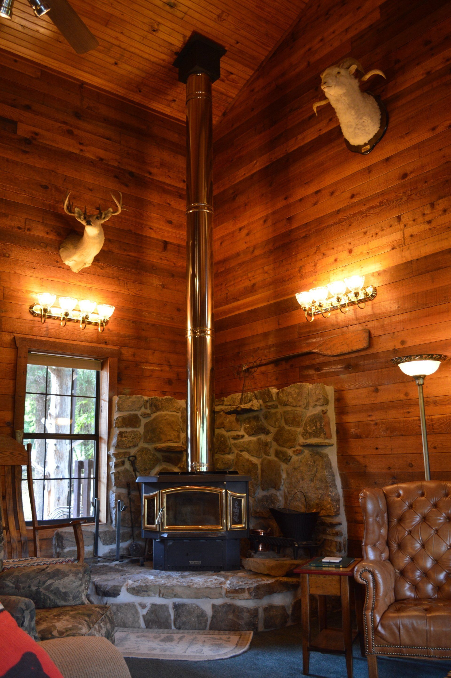 Rustic log cabin interior with a wood stove, stone hearth, mounted deer head, and leather chair
