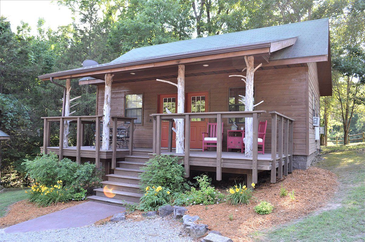 Rustic wooden cabin porch with steps, railing, and red chairs surrounded by trees