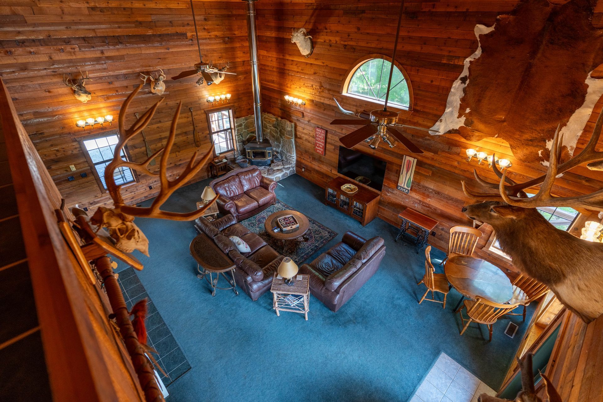 Cozy wooden cabin loft with blue carpet, seating area, hanging lights, and arched window