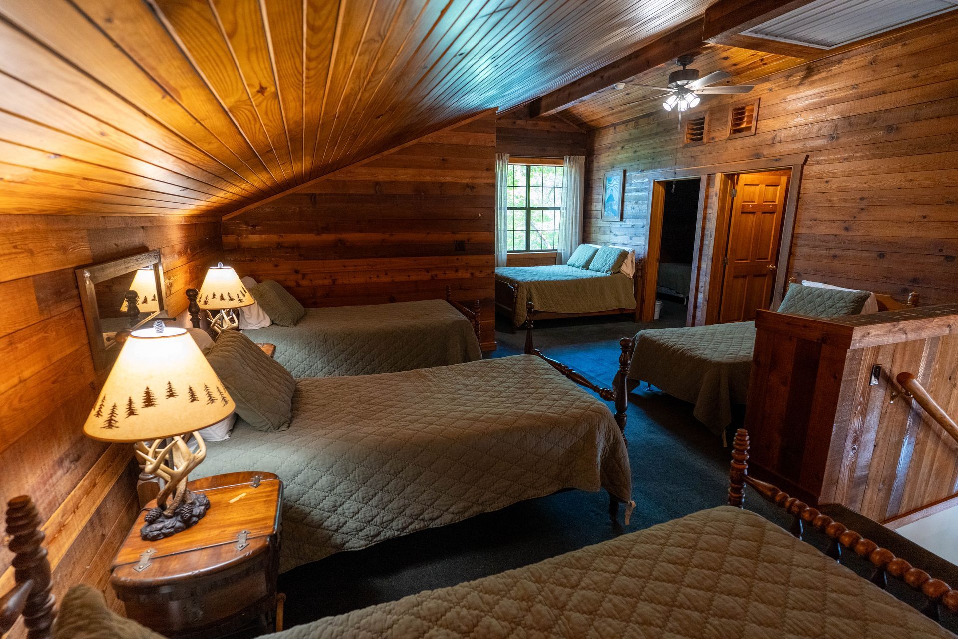 Rustic cabin bedroom with wood-paneled walls, multiple beds, lamps, and a window view