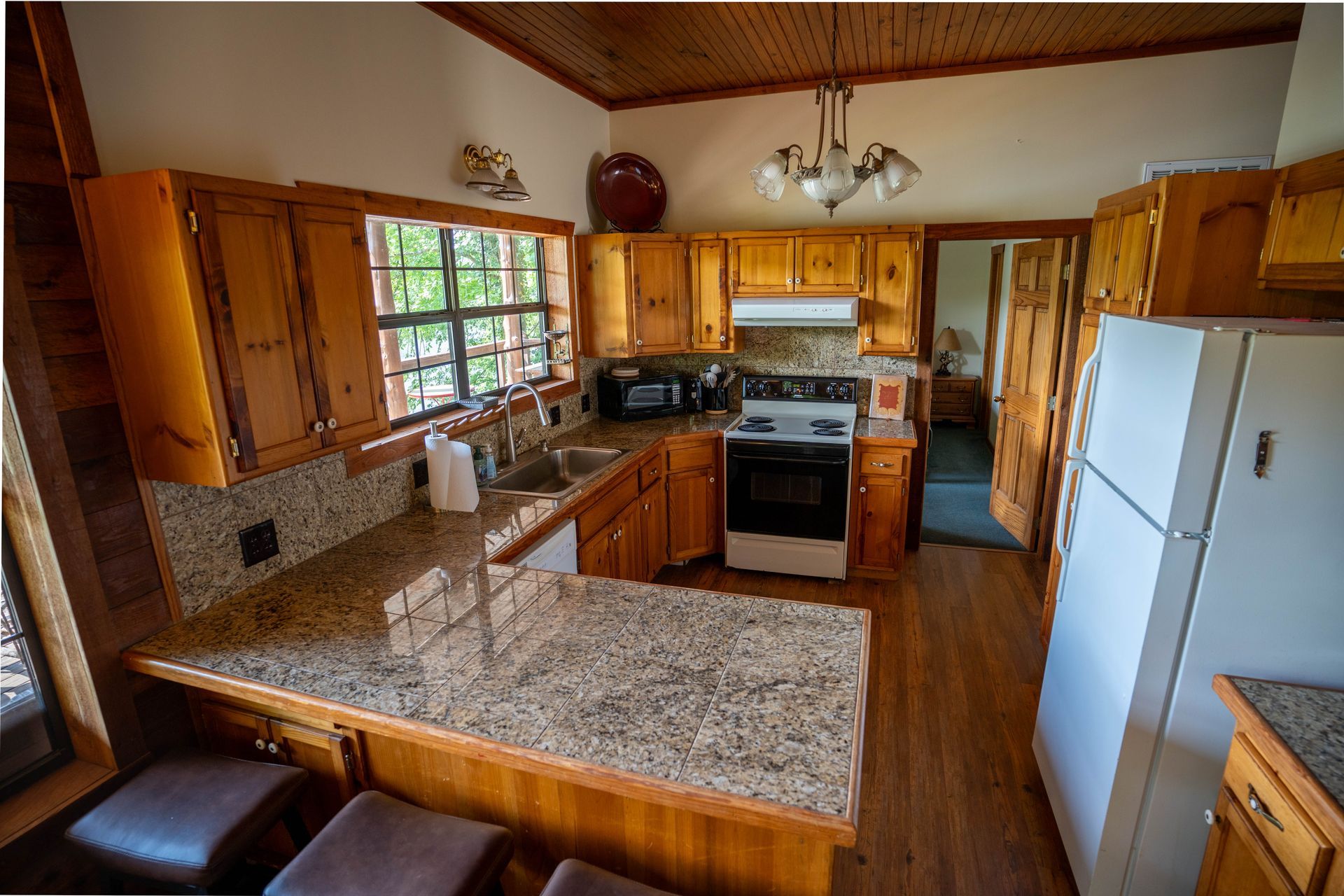Wooden kitchen with granite counters, white appliances, and a large window over the sink