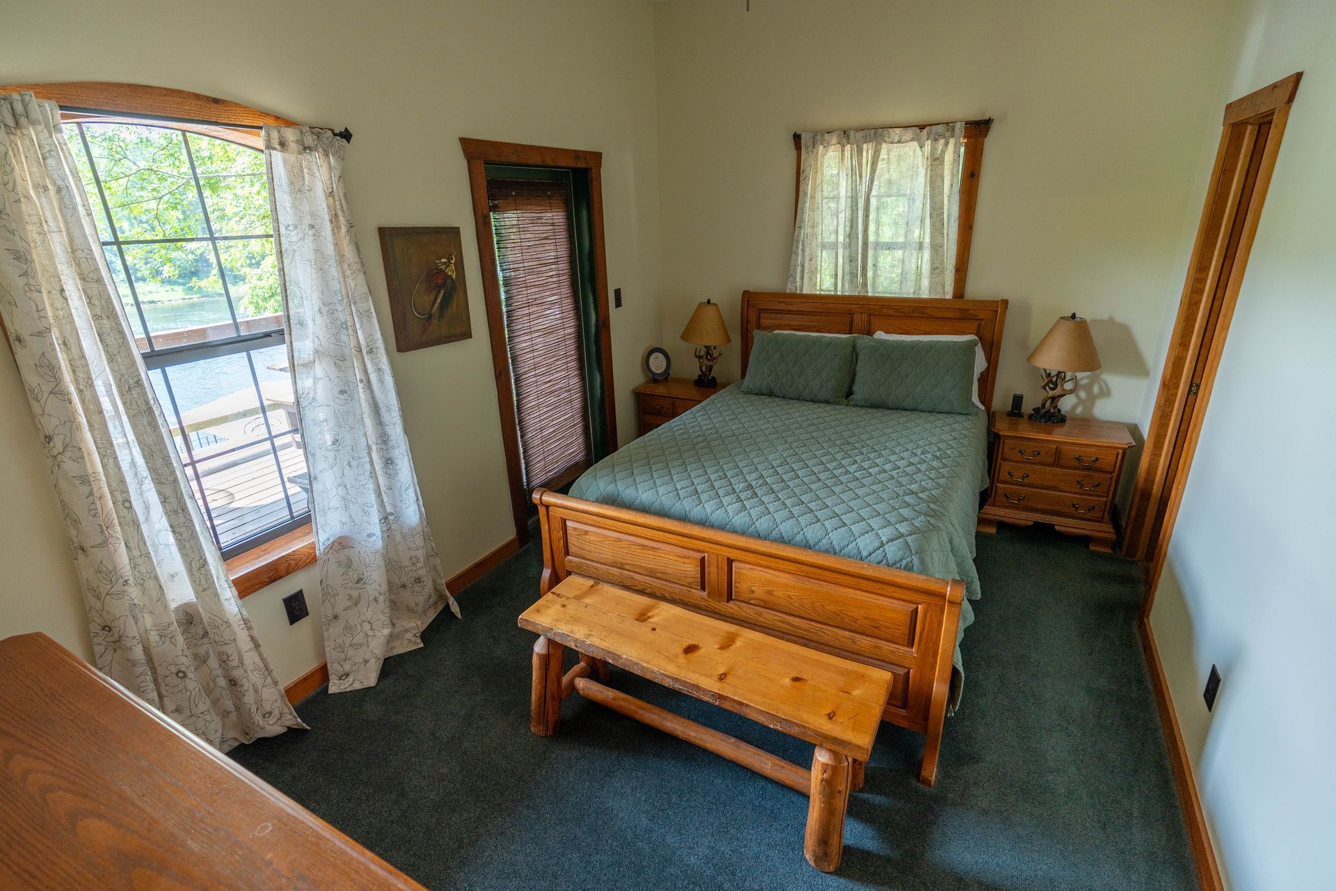 Small bedroom with a wooden bed, green carpet, and two curtained windows.
