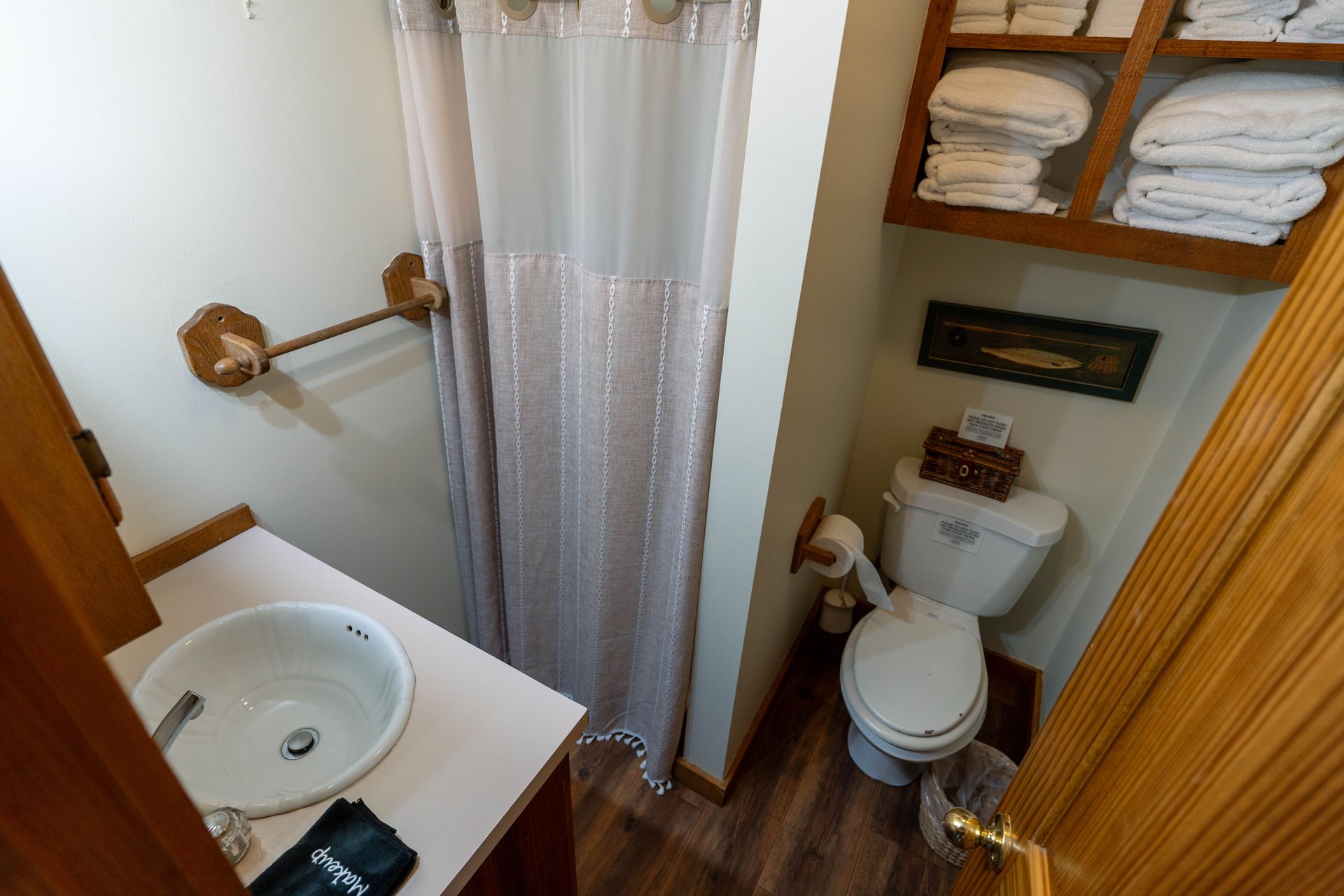 Small bathroom with sink, toilet, shower curtain, and stacked towels on shelves.