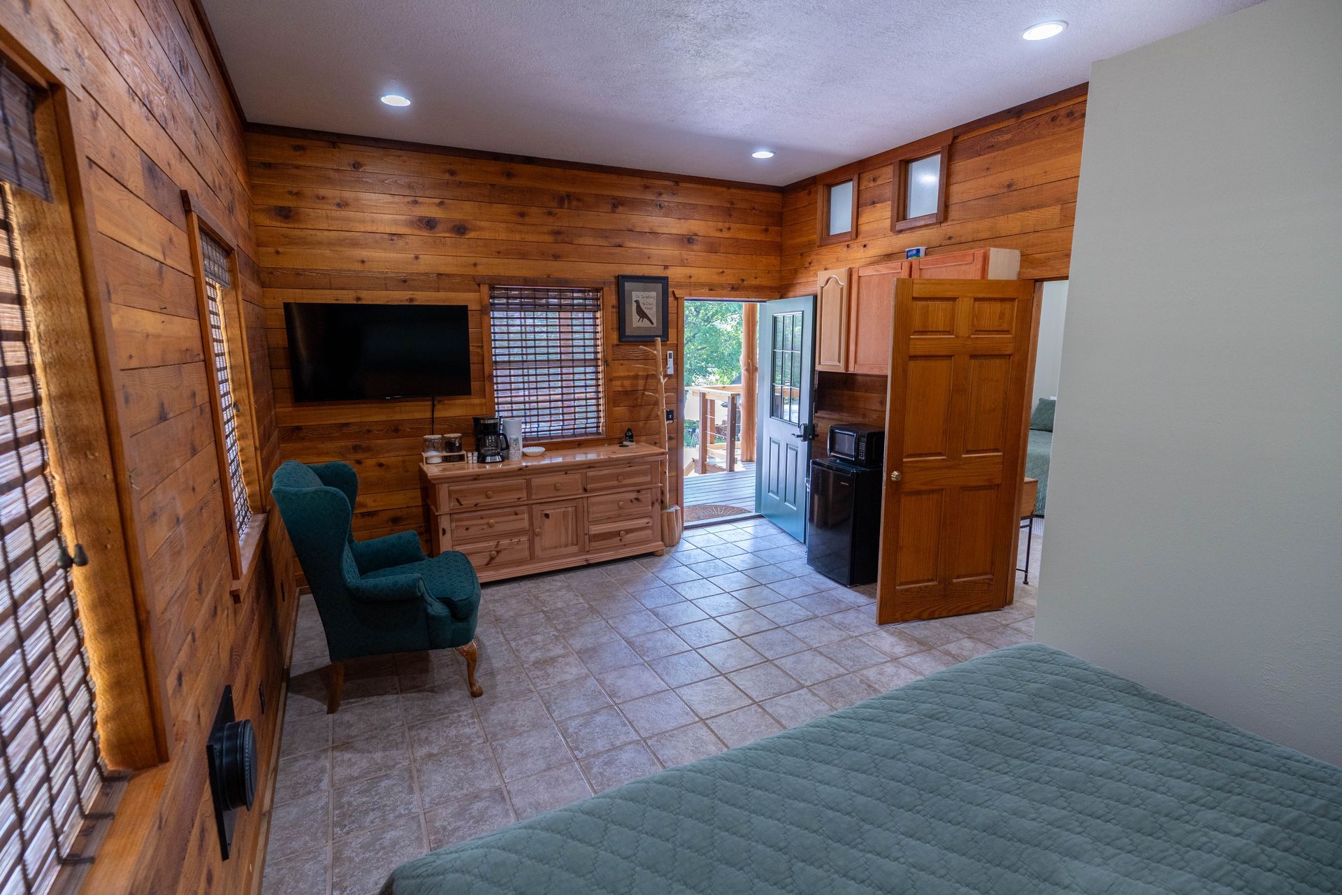Wood-paneled bedroom with tiled floor, bed, TV, chair, and open doorway to another room