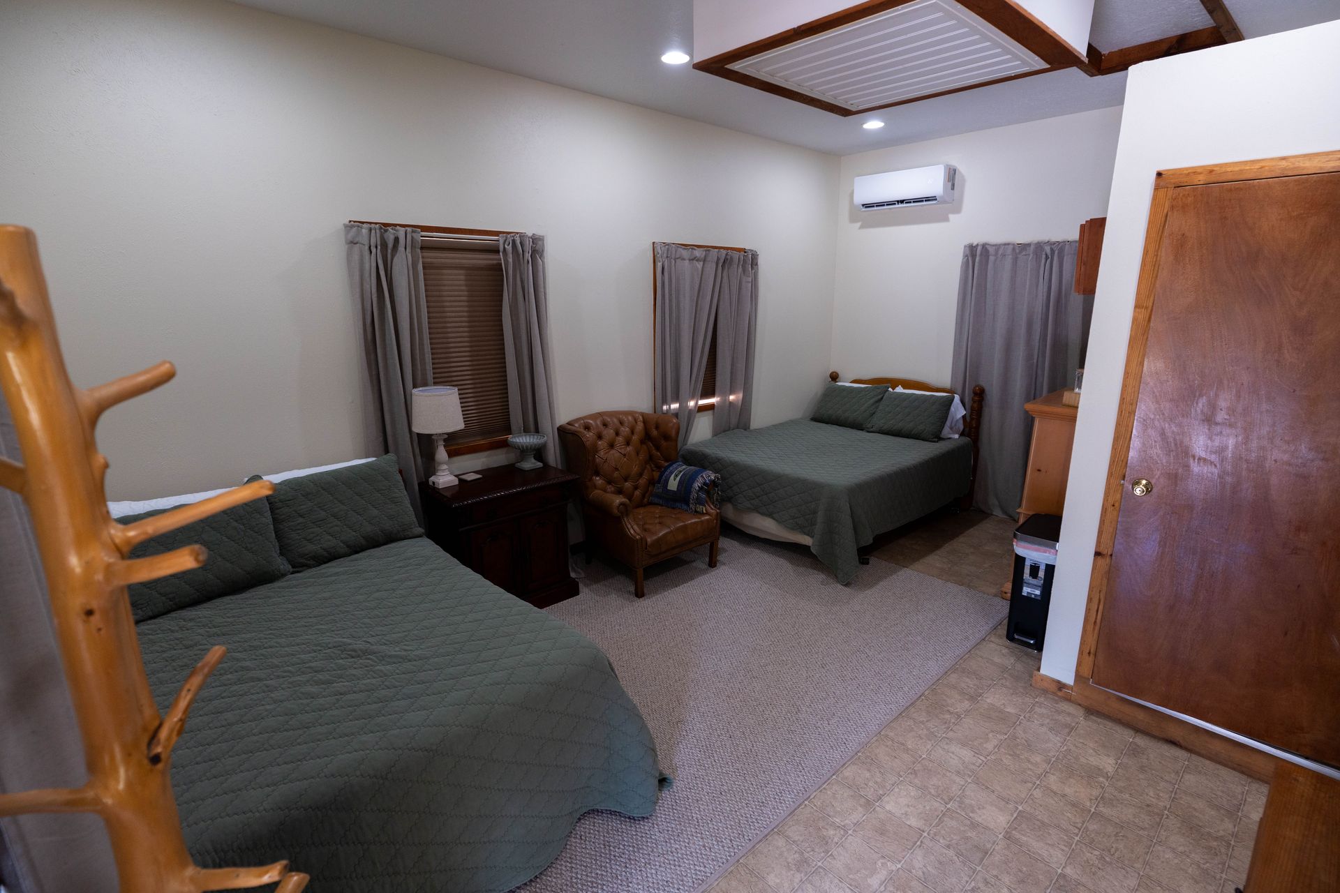Small bedroom with two twin beds, a wicker chair, curtains, and a wooden door.