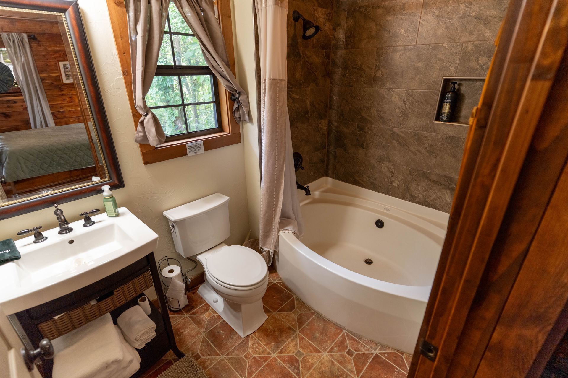 Small bathroom with sink, toilet, and corner bathtub, featuring wood trim and tiled floor