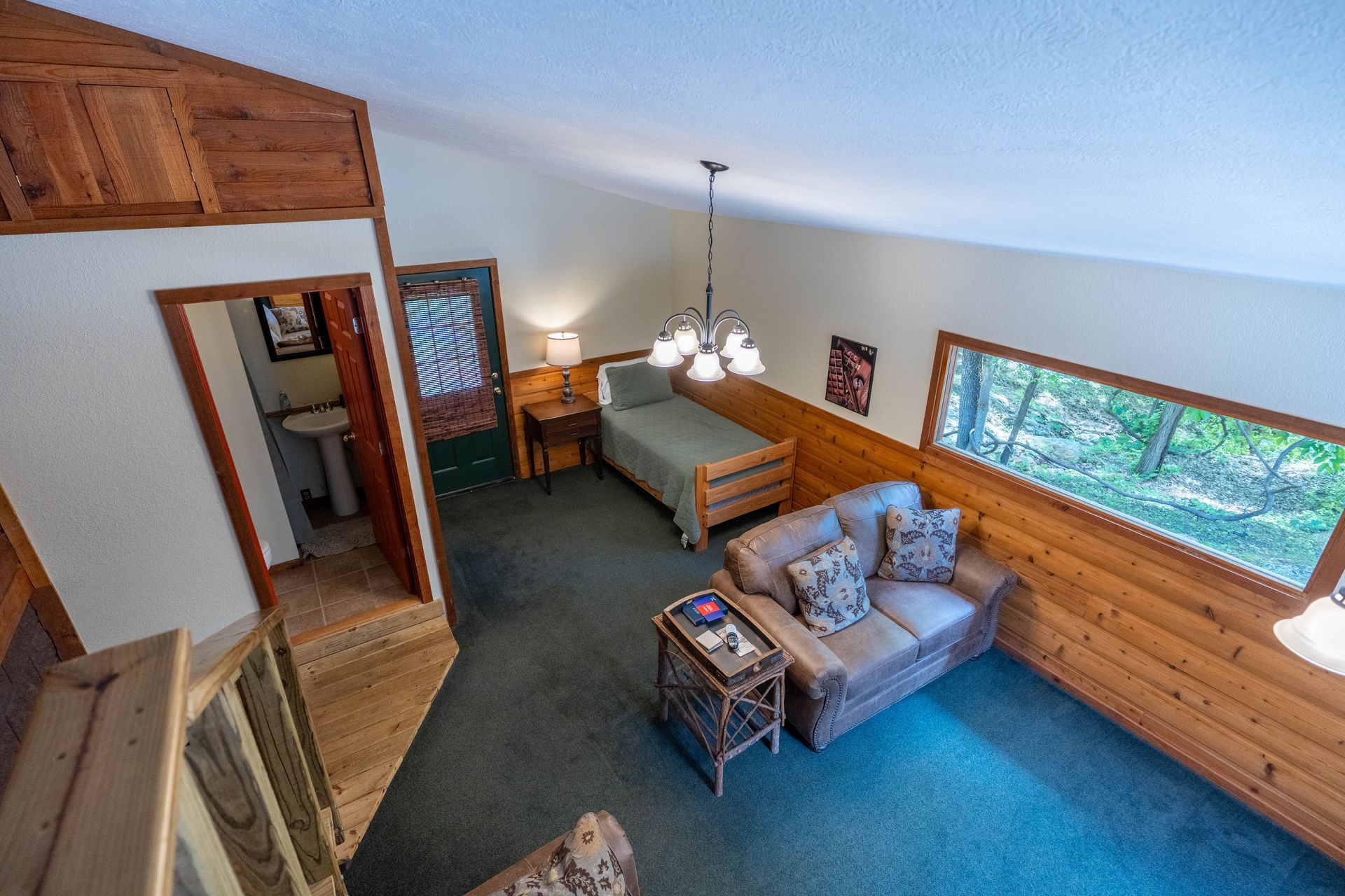 High-angle view of a cozy living room with blue carpet, wood-paneled walls, sofa, and large window.