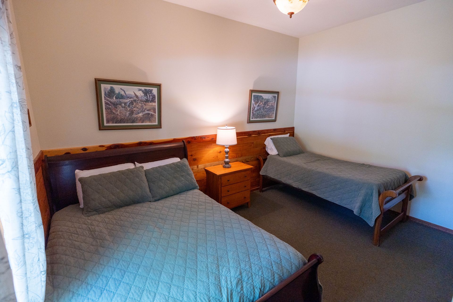 Bedroom with two twin beds, blue quilts, wooden nightstand, and framed wall art