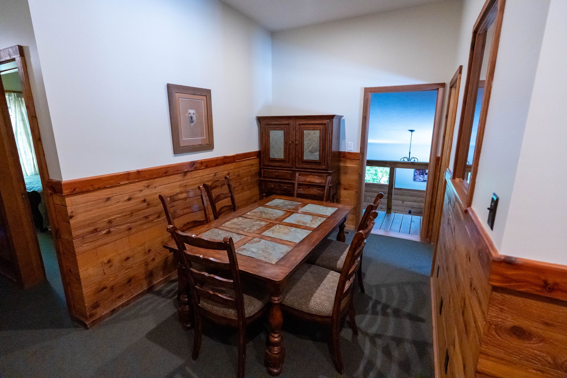 Wood-paneled dining room with a wooden table, chairs, and a doorway opening to a bright balcony view
