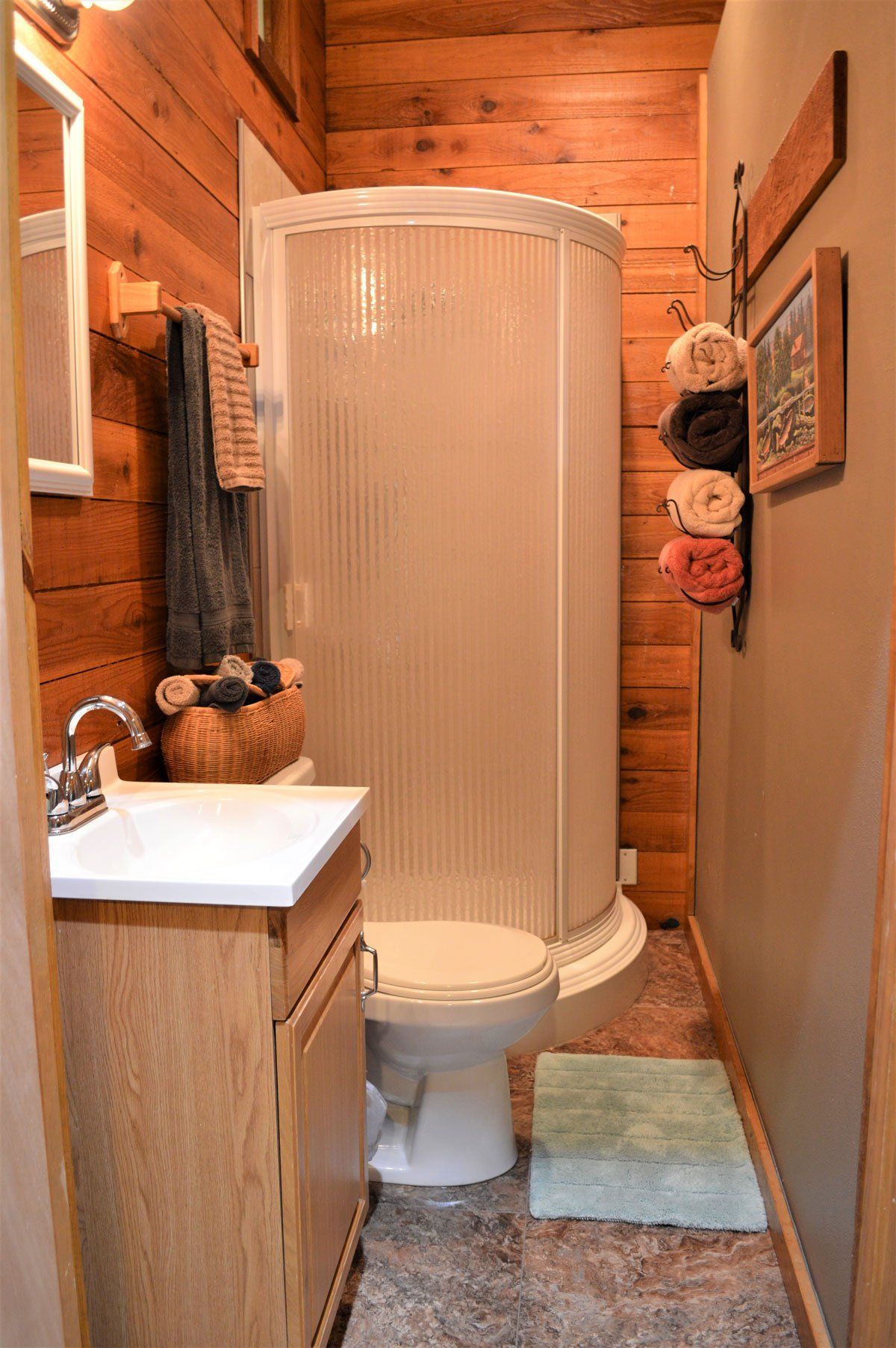 Small rustic bathroom with a white shower booth, sink, and towels on wooden walls.