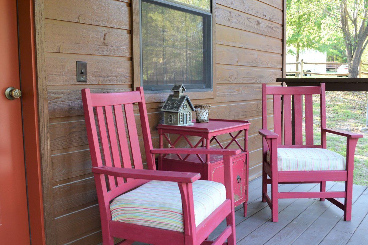 Two pink wooden chairs beside a small table on a covered porch